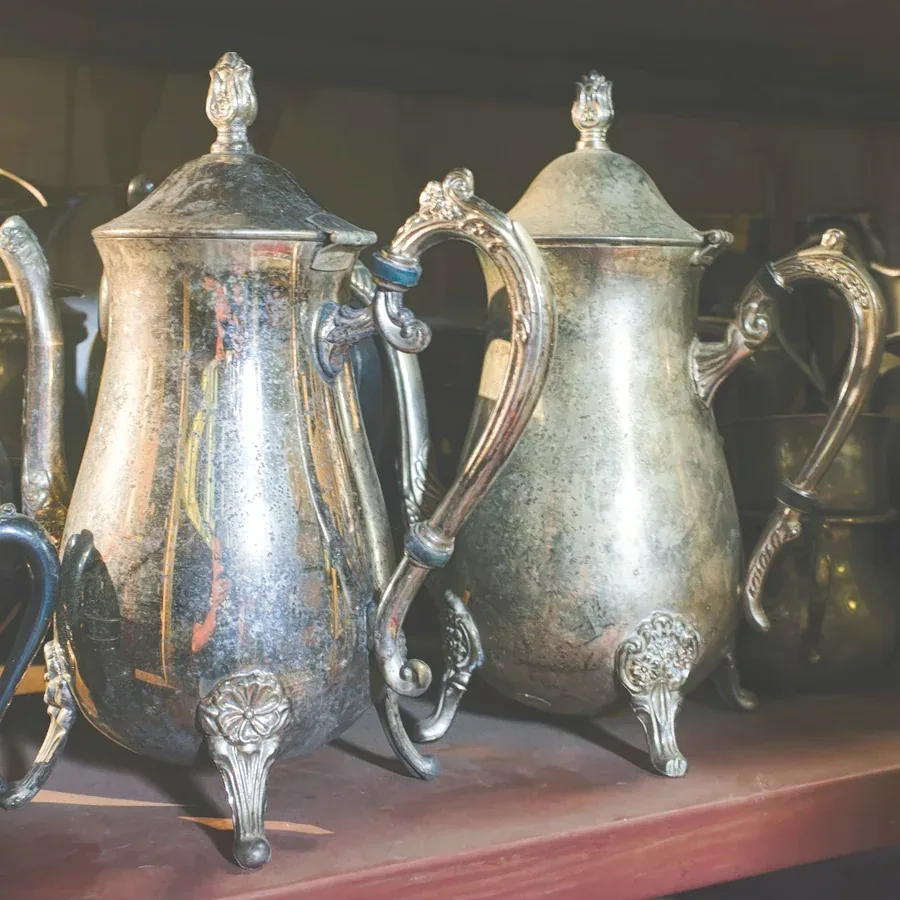 A shelf of antique silver coffee pots and pitchers