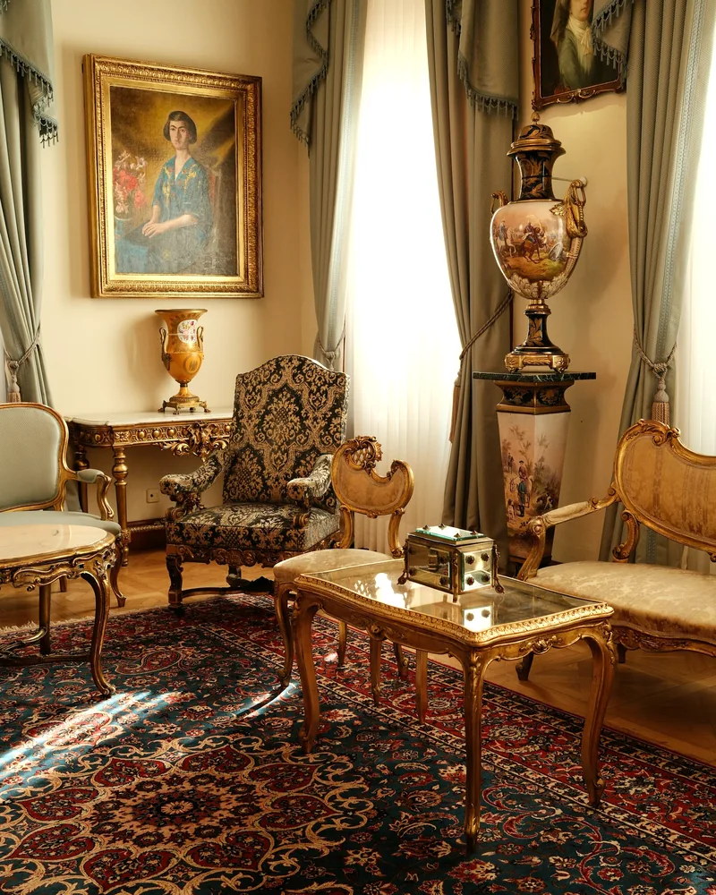 A bright parlor with carved antique chairs, oil paintings and an Oriental rug